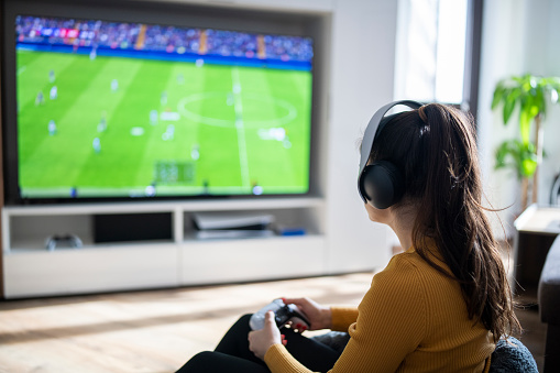 Rear view of woman playing football game on a gaming console at home.