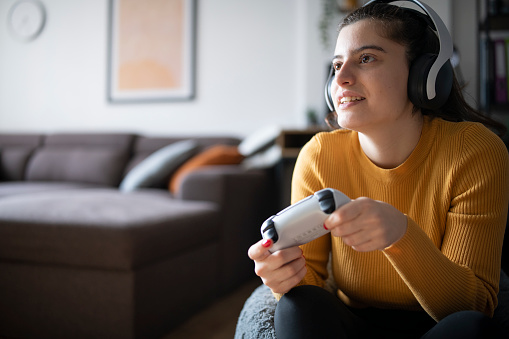 Young woman with wireless headphones holding a joystick and playing video games.