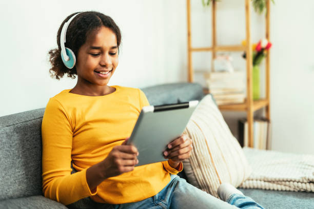 istock Happy African young girl using digital tablet technology sitting on couch at home. 1464190357