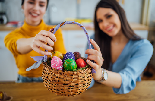 Young cheerful female friends with a basket full of colored Easter eggs at home on Easter day