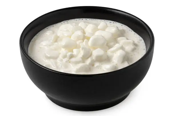 Chunky cottage cheese with whey in a black ceramic bowl isolated on white.