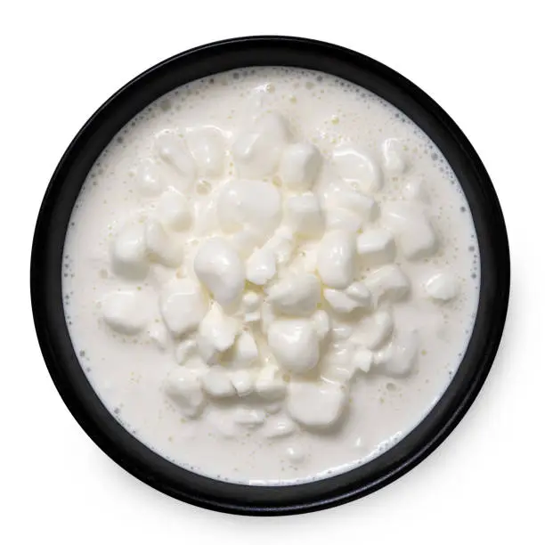 Chunky cottage cheese with whey in a black ceramic bowl isolated on white. Top view.