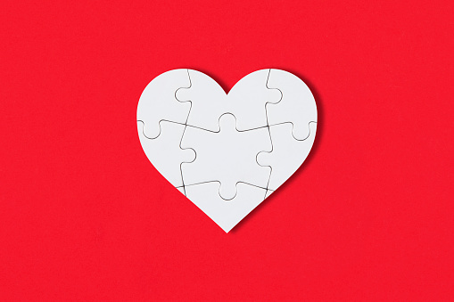 White puzzle pieces comes together as heart shape on red background