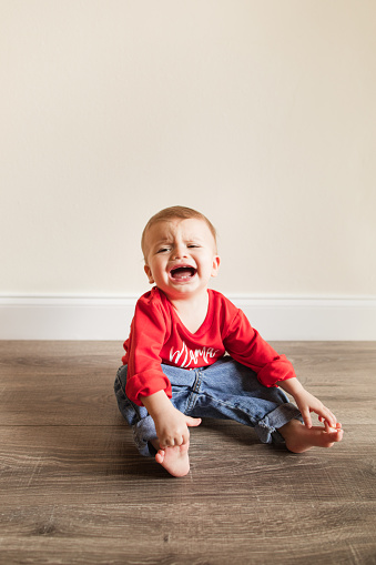 A Cute 13-Month-Old Christmas Baby Boy with 12 Toes, Barefoot, Dressed in Vintage Jeans & a Red Sweater That Says 