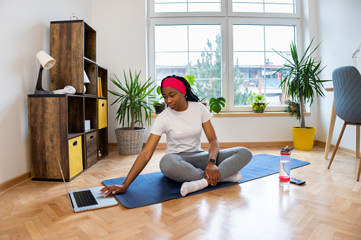 Young woman of Black ethnicity, practicing yoga at home, while follow online yoga tutorial/class on laptop