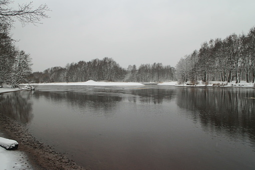 river winter landscape, the banks of the river are covered with white snow, the water is covered with the first ice
