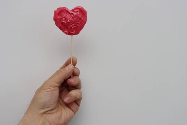 istock A man's hand holds a red heart-shaped lollipop. 1464200479