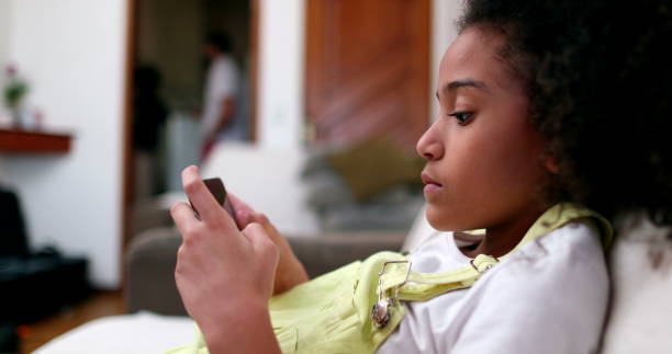 istock Little black girl using smartphone device at home sofa. African ethnicity 1464204034