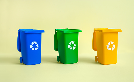 Blue, yellow and green tank for separate garbage collection on the yellow background, waste recycling and conservation of the environment concept