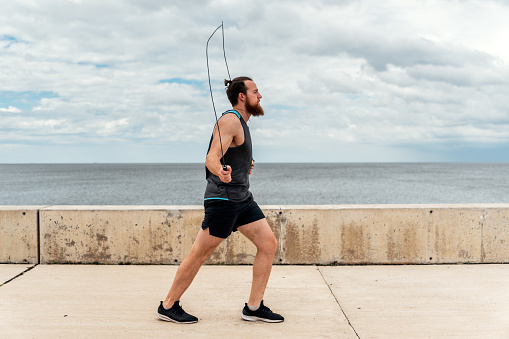 Focused bearded man using jumping rope outdoors and looking at front.