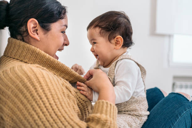 Mother Playing at Home with her Baby Stock photo of young mother sharing cute moment with her little baby in the living room. mom and baby eye contact stock pictures, royalty-free photos & images