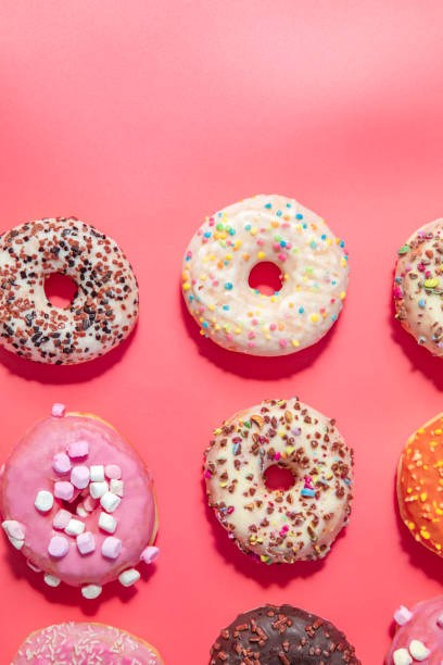 istock Donuts with icing on pastel pink background. Sweet donuts. top view assorted with various chocolate glazed and sprinkles, sugar sweets concept 1464208570