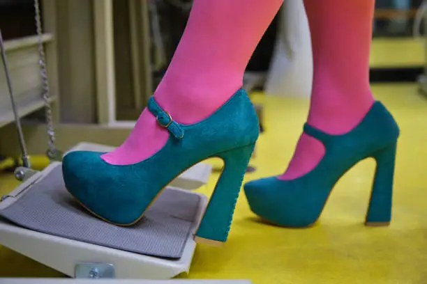 Close up of pink tights and green high heels depressing sewing machine pedal in a sewing workshop.