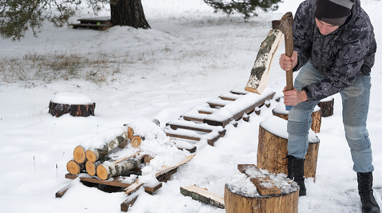 A man is chopping firewood with an axe in winter outdoor in the snow. Alternative heating, wood harvesting, energy crisis