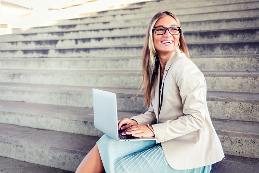 Woman sitting on steps outdoors and using laptop. Businesswoman working on laptop while sitting on steps outside.