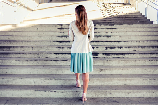 Rear view of young business woman moving up on stairs. Back view of female entrepreneur going to work in the city. Copy space.