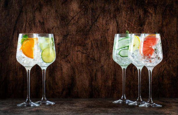 istock Gin and tonic cocktails set. Alcoholic drinks with lime, lemon, grapefruit, cucumber, soda and spicy herbs in wine glasses, wooden background. Summer cocktail party 1464223755