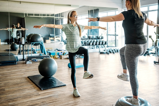 Female trainer instructing a woman exercising on bosu ball at gym