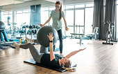 Rehabilitation specialist instructing a woman exercising with a fitness ball at the gym