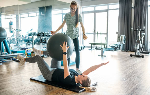 specjalista rehabilitacji instruujący kobietę ćwiczącą piłką fitness na siłowni - pilates health club gym exercising zdjęcia i obrazy z banku zdjęć