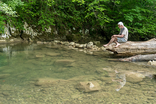 Senior men relaxing on the rock at rapid of cold river in forest at Šmarjetske toplice - spa