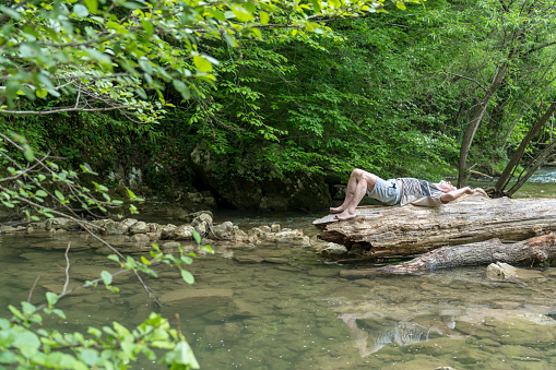 Senior men relaxing on the large log at rapid of cold river in forest at Šmarjetske toplice - spa