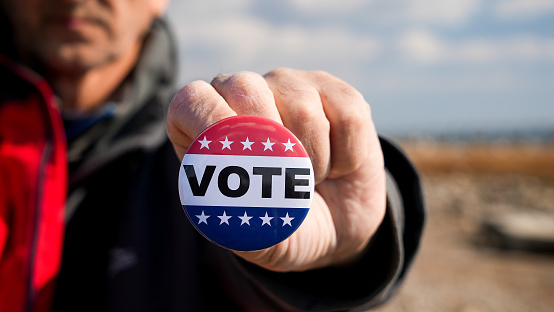 Man is holding patriotic button with Vote text outside