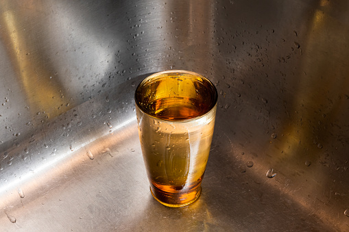 Full glass of water sitting in the corner of a stainless steel sink with lots of reverse copy space.
