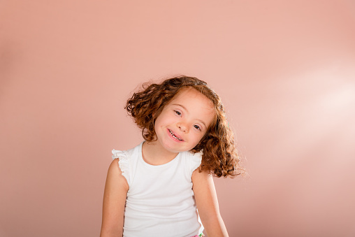 Beautiful red-haired little girl posing for the camera. Isolated on salmon background.