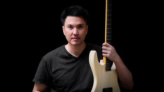 portrait of asian young handsome musician posing with white electric guitar, isolated on black