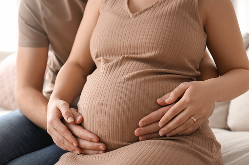 Man touching his pregnant wife's belly at home, closeup