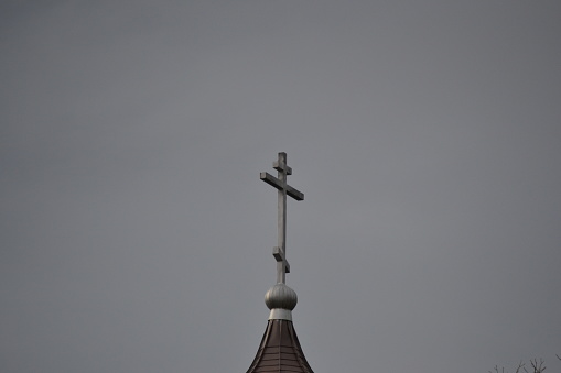 With an autumn dusk turned orange by harvest dust, a wood church steeple and cross is shown against the sky. Horizontal with copy space.