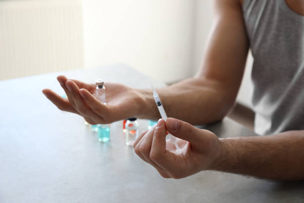 man with syringe and vial at grey table, closeup. doping concept - steroids imagens e fotografias de stock