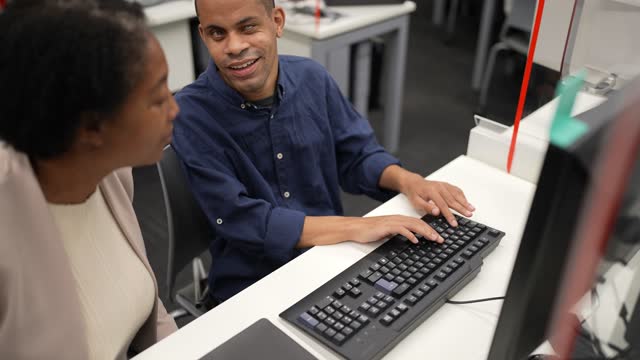 Visually impaired man using the computer with help from a mature woman at university