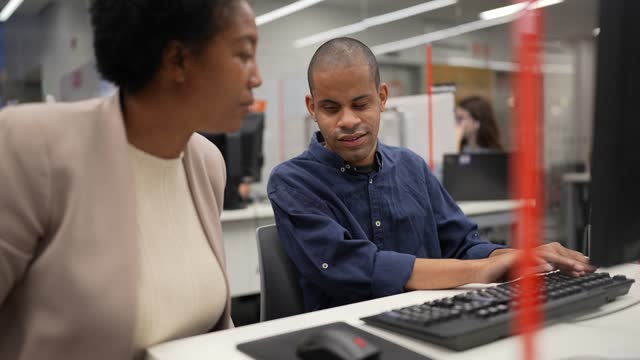 Visually impaired man using the computer with help from a mature woman at university