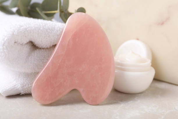 istock Rose quartz gua sha tool, jar of cream and towel on grey table, closeup 1464239930