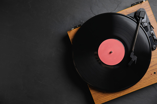 Modern vinyl record player with disc on black background, top view. Space for text