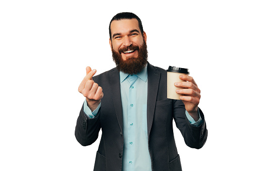 Smiling bearded man shows the Korean heart gesture and holds a take away cup over white background.