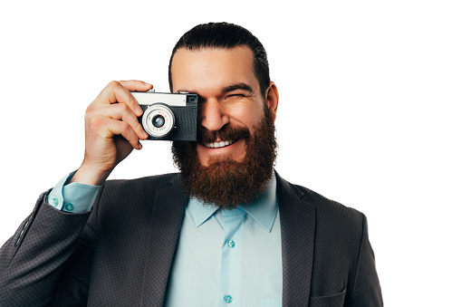 Cheerful handsome bearded man is looking through camera he is holding over white background.