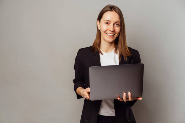 Modern smiling woman standing in a studio is holding an opened laptop. stock photo