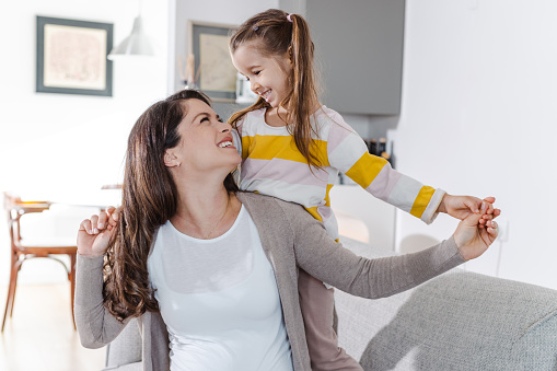 Beautiful pregnant woman enjoying with her cute little daughter at home