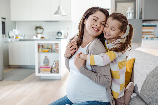 Pregnant woman with her children relaxing in bed. Loving mother and toddlers together at home. Little kids hold hands on pregnant belly of mom. Third pregnancy. Maternity, family, parenting concept.