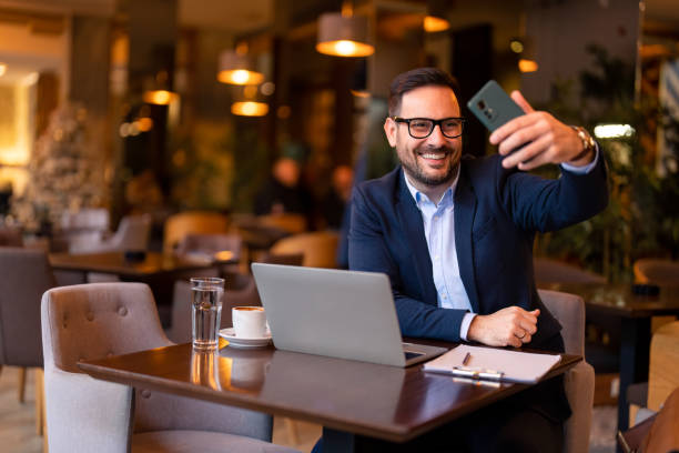 istock Smiling handsome millennial man using smartphone to take a self portrait picture while working on laptop in Cafe or restaurant 1464249695