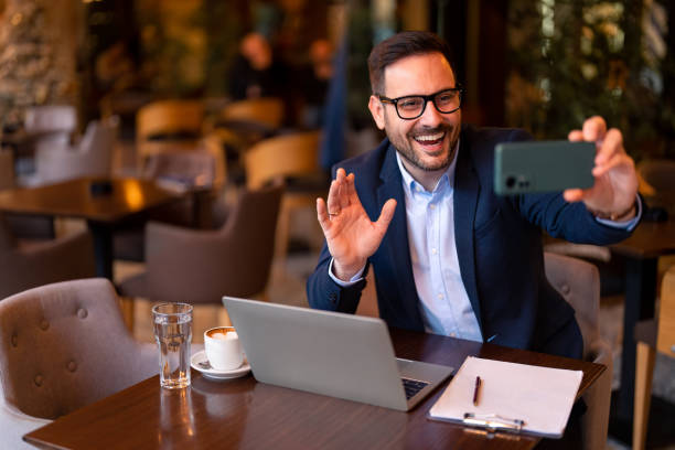 istock Smiling business man waving at mobile phone camera using smart phone to communicate online, make video call 1464249715