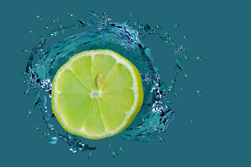 Yellow lemon in bright azure water with splashes in different directions.