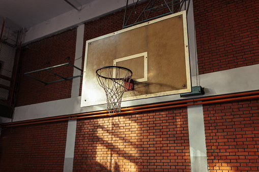 A basketball board with the rim and the net in an empty indoors basketball court.