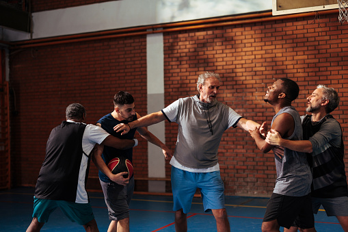 A senior man is separating his younger friends who are fighting at their recreational basketball game.