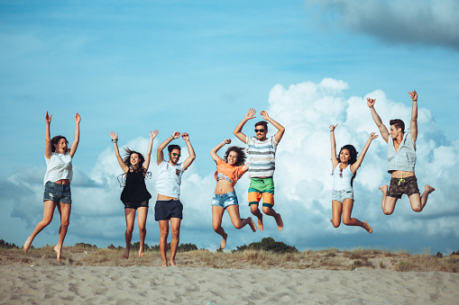 A group of teenagers enjoy a summer day outdoors at sea. The friends play dance and relax on a beach during summer vacation