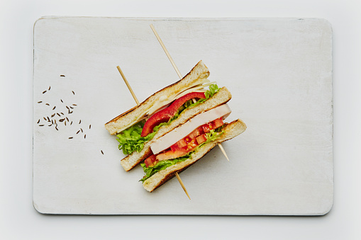 Solo club sandwich on a handmade ceramic plate, made of fresh bread, lettuce, ham, cheese, red pepper, tomato, mayo and ketchup. Isolated on a white background, top view image with a large copy space area