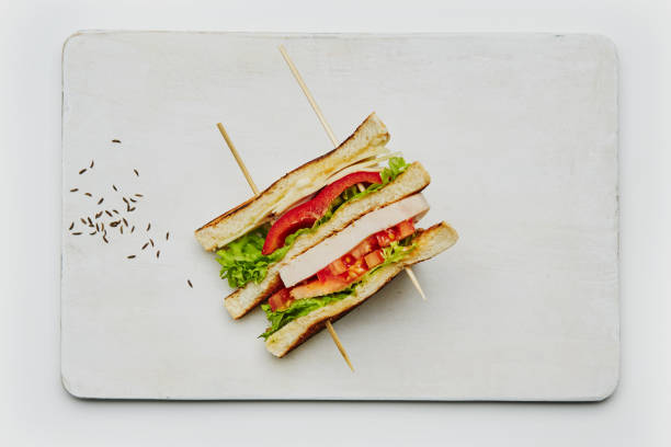 Club sandwich on a white background Solo club sandwich on a handmade ceramic plate, made of fresh bread, lettuce, ham, cheese, red pepper, tomato, mayo and ketchup. Isolated on a white background, top view image with a large copy space area sandwich club sandwich lunch restaurant stock pictures, royalty-free photos & images